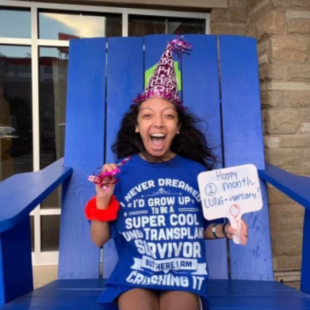 Nicole smiling sitting on blue chair with one month lung-anniversary sign