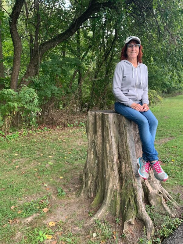 Sarita siting on tree stump and smiling.