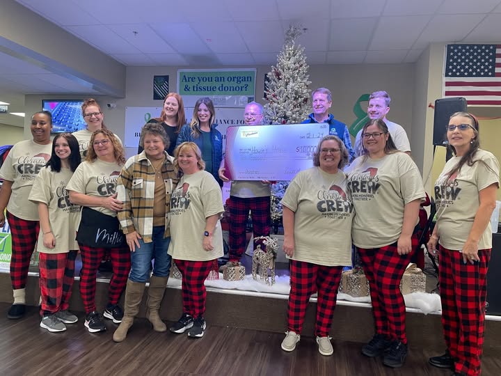 Group in "Christmas Crew" shirts and red and black pajama pants gathered around a giant check for $10,000 made out to Howie's House