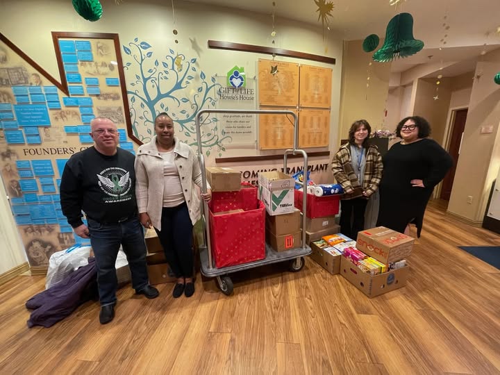 Four people standing next to cart of donated pantry staples from the wish-list drive in the Howie's House entrance