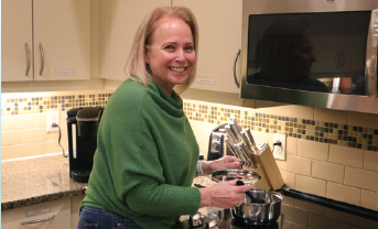 Louanne in the Kitchen, stirring a pot with a large spoon and smiling at the camera.