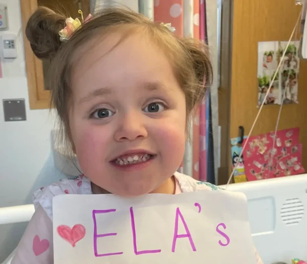 Pictured is Ela, a transplant recipient smiling and holding a sign.